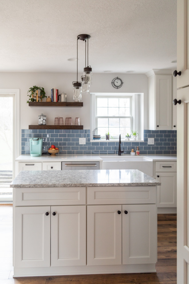 This is an example of a large contemporary u-shaped eat-in kitchen in Other with a farmhouse sink, shaker cabinets, white cabinets, quartz benchtops, blue splashback, glass tile splashback, stainless steel appliances, medium hardwood floors, with island, brown floor and grey benchtop.