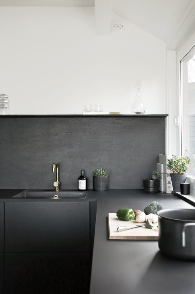 Photo of a small scandinavian u-shaped kitchen in Other with a drop-in sink, flat-panel cabinets, wood benchtops, black splashback, light hardwood floors and with island.