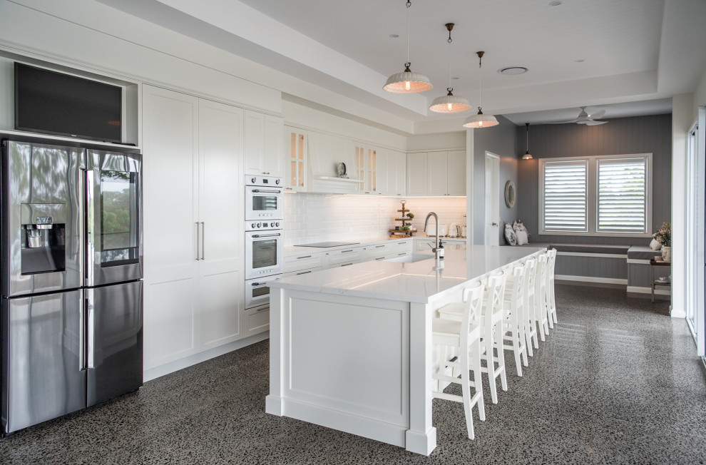 Photo of a transitional u-shaped eat-in kitchen in Sunshine Coast with a farmhouse sink, shaker cabinets, white cabinets, quartz benchtops, white splashback, subway tile splashback, stainless steel appliances, with island, grey floor and white benchtop.