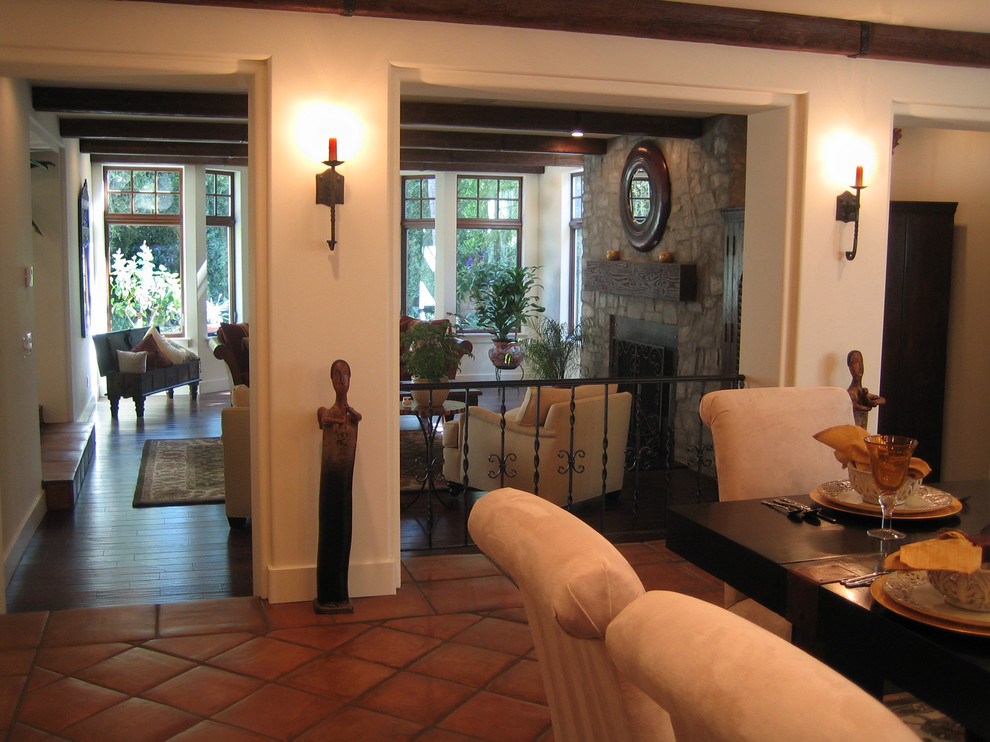 Photo of a large mediterranean separate dining room in Los Angeles with white walls, terra-cotta floors, a standard fireplace and a stone fireplace surround.