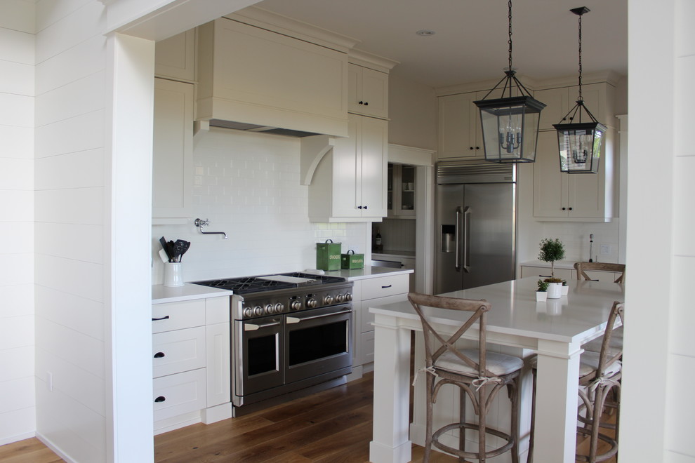 Example of a large transitional l-shaped eat-in kitchen design in Toronto with an undermount sink, shaker cabinets, white cabinets, quartz countertops, white backsplash, stainless steel appliances and an island