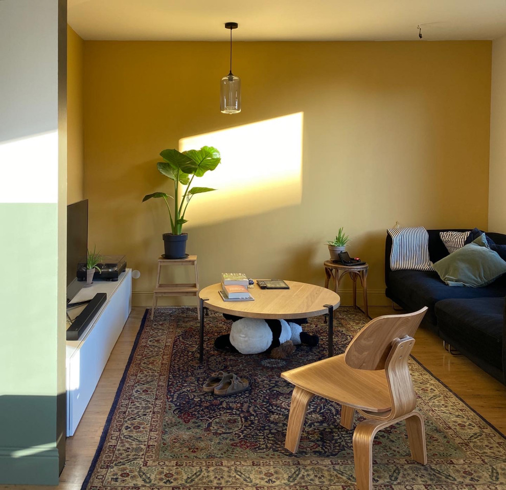 Idées déco pour un petit salon éclectique ouvert avec un mur jaune, parquet clair, aucune cheminée, un téléviseur indépendant et canapé noir.