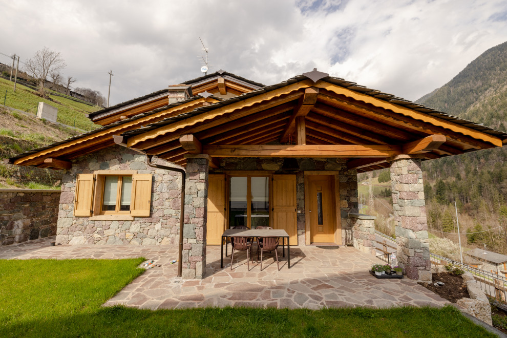 Réalisation d'une grande façade de maison multicolore chalet en pierre et bardeaux à un étage avec un toit à deux pans et un toit marron.