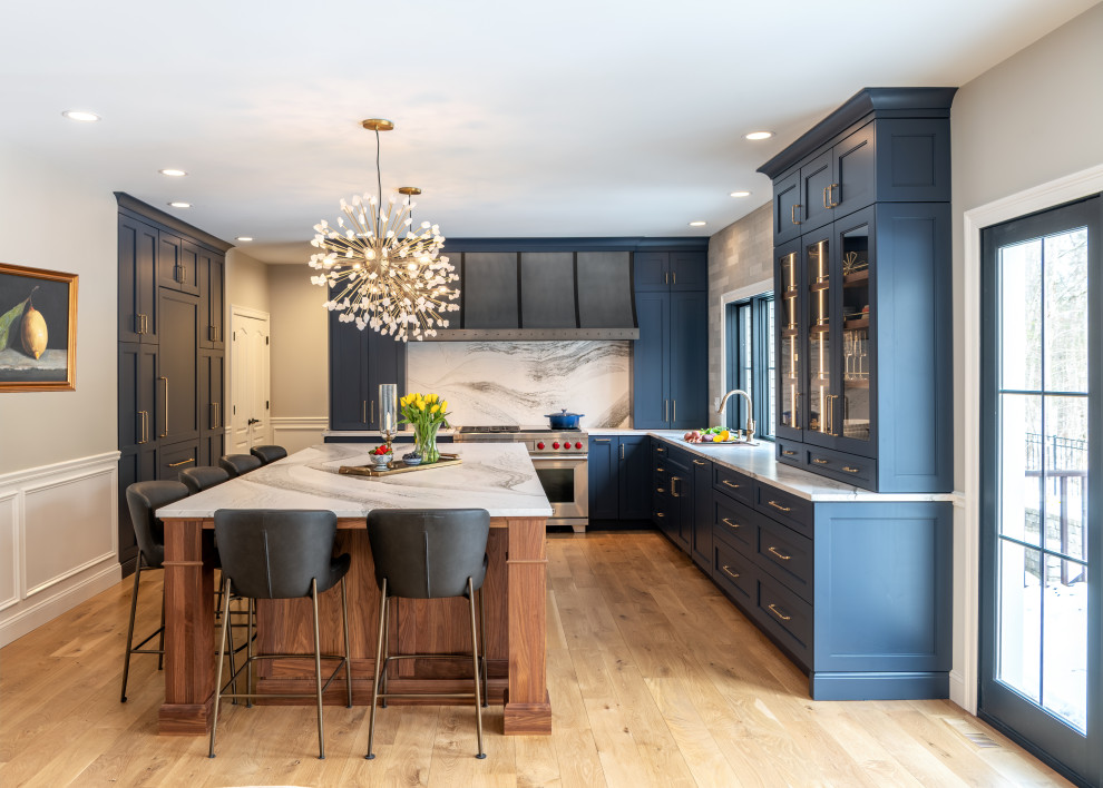 Example of a transitional u-shaped medium tone wood floor and brown floor kitchen design in Boston with recessed-panel cabinets, blue cabinets, white backsplash, stone slab backsplash, stainless steel appliances, an island and white countertops