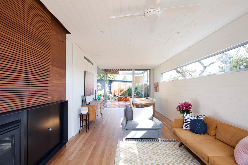 Photo of a mid-sized contemporary open concept living room in Sydney with white walls, light hardwood floors, a standard fireplace, a wood fireplace surround and a concealed tv.