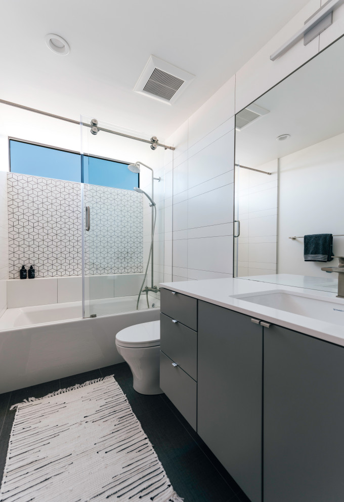 Источник вдохновения для домашнего уюта: маленькая ванная комната в стиле ретро с плоскими фасадами, серыми фасадами, ванной в нише, душем над ванной, унитазом-моноблоком, белой плиткой, керамической плиткой, белыми стенами, полом из керамогранита, душевой кабиной, врезной раковиной, столешницей из искусственного кварца, серым полом, душем с раздвижными дверями, белой столешницей, тумбой под одну раковину и подвесной тумбой для на участке и в саду