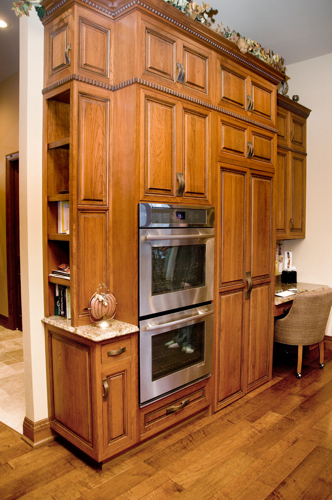 Open concept kitchen - large transitional l-shaped open concept kitchen idea in Cedar Rapids with a farmhouse sink, raised-panel cabinets, medium tone wood cabinets, granite countertops, stainless steel appliances and an island