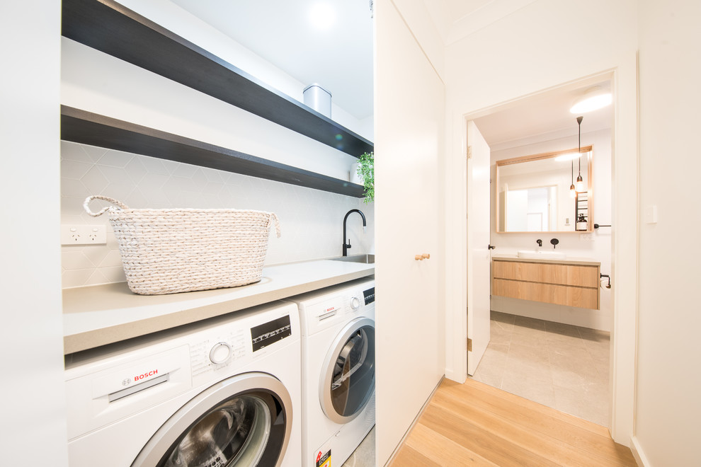 Inspiration for a mid-sized contemporary single-wall laundry cupboard in Central Coast with an integrated sink, flat-panel cabinets, white cabinets, quartz benchtops and a side-by-side washer and dryer.