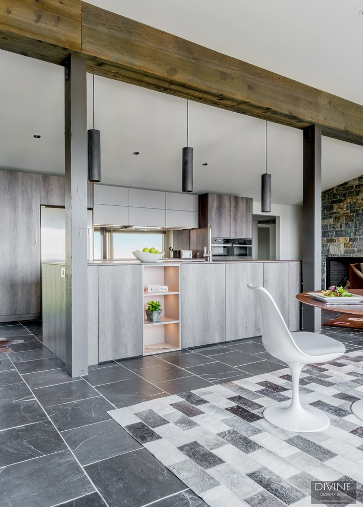 Large eclectic single-wall open plan kitchen in Boston with an undermount sink, flat-panel cabinets, dark wood cabinets, granite benchtops, metallic splashback, glass sheet splashback, stainless steel appliances, slate floors, with island, grey floor and brown benchtop.