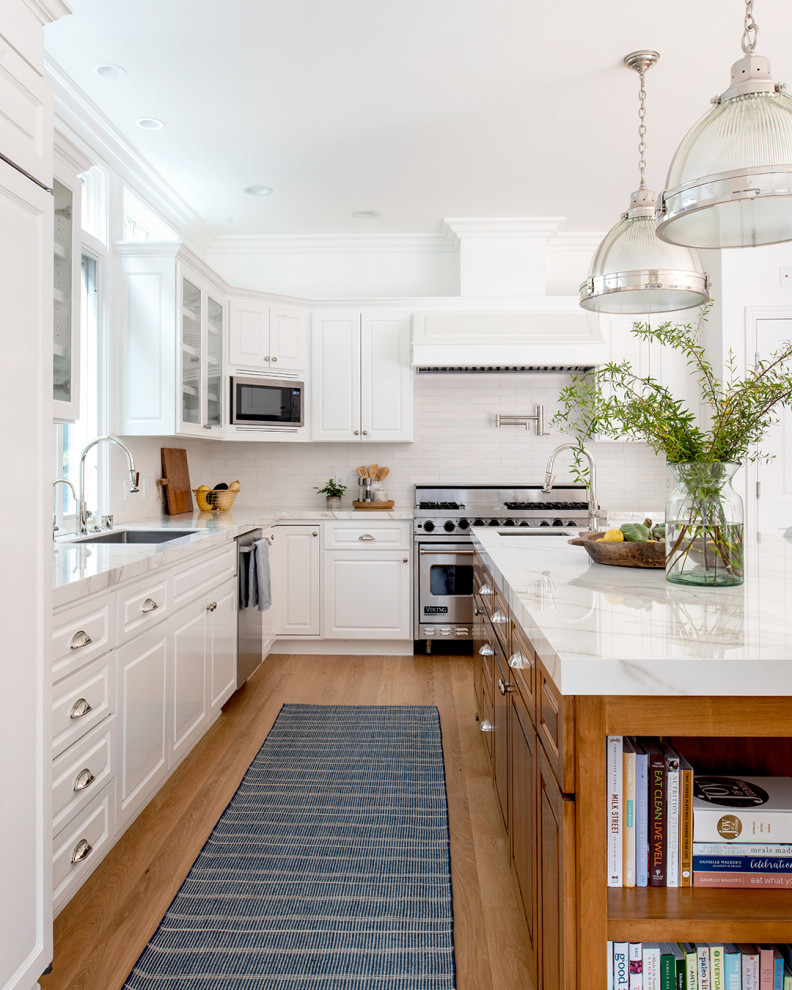 This is an example of a traditional kitchen in Los Angeles with beaded cabinets, white splashback, porcelain splashback, stainless steel appliances, light hardwood flooring, an island and white worktops.