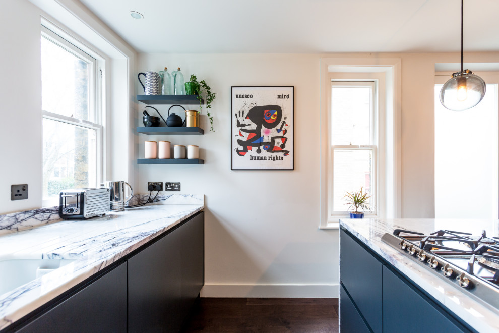 This is an example of a small traditional single-wall separate kitchen in London with an integrated sink, flat-panel cabinets, black cabinets, marble benchtops, stainless steel appliances, dark hardwood floors, with island, brown floor and multi-coloured benchtop.