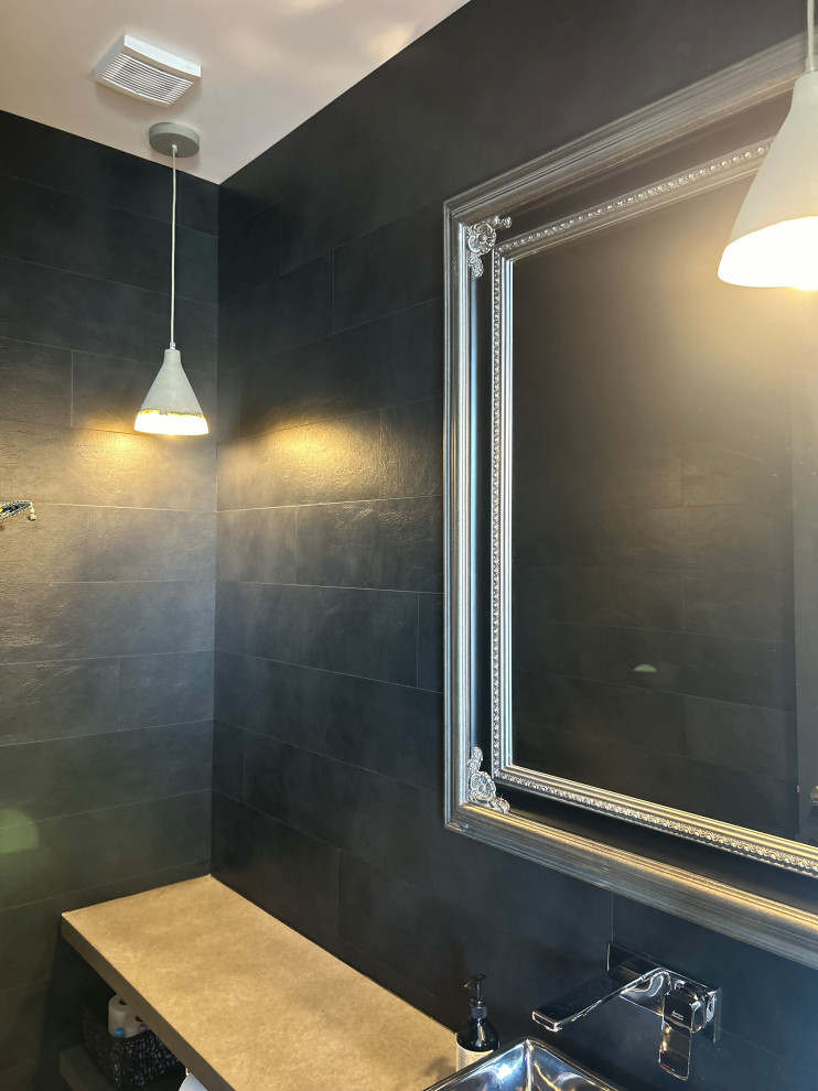 This is an example of a small industrial cloakroom in Hamilton with a one-piece toilet, black tiles, black walls, medium hardwood flooring, a vessel sink, brown floors, grey worktops, panelled walls and a floating vanity unit.