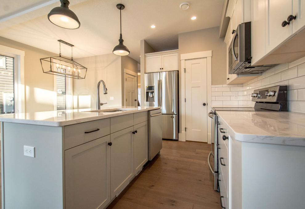 Eat-in kitchen - mid-sized transitional single-wall medium tone wood floor and brown floor eat-in kitchen idea in Calgary with an undermount sink, shaker cabinets, gray cabinets, marble countertops, white backsplash, subway tile backsplash, stainless steel appliances, an island and white countertops
