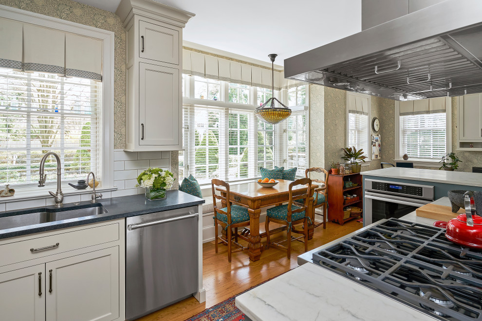 Enclosed kitchen - large transitional l-shaped medium tone wood floor and brown floor enclosed kitchen idea in Philadelphia with a double-bowl sink, recessed-panel cabinets, green cabinets, soapstone countertops, beige backsplash, ceramic backsplash, stainless steel appliances, an island and beige countertops