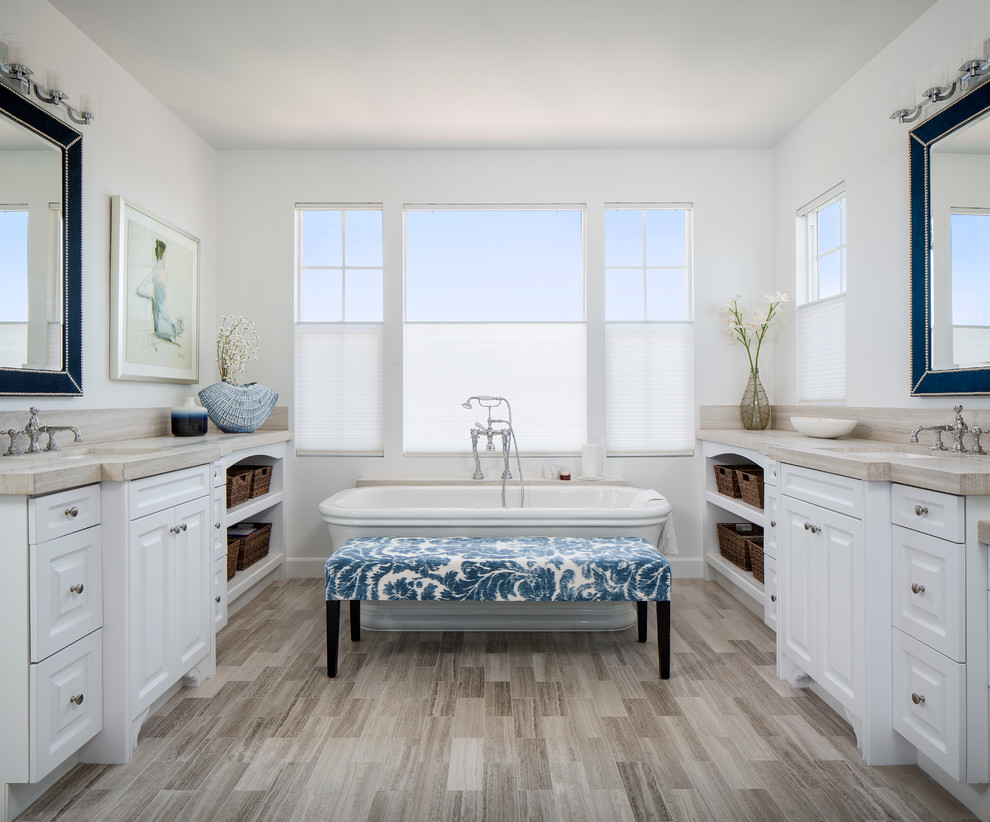 Inspiration for a large beach style master bathroom in San Francisco with raised-panel cabinets, white cabinets, a freestanding tub, gray tile, porcelain tile, white walls, an undermount sink, wood benchtops, a two-piece toilet, light hardwood floors and beige benchtops.