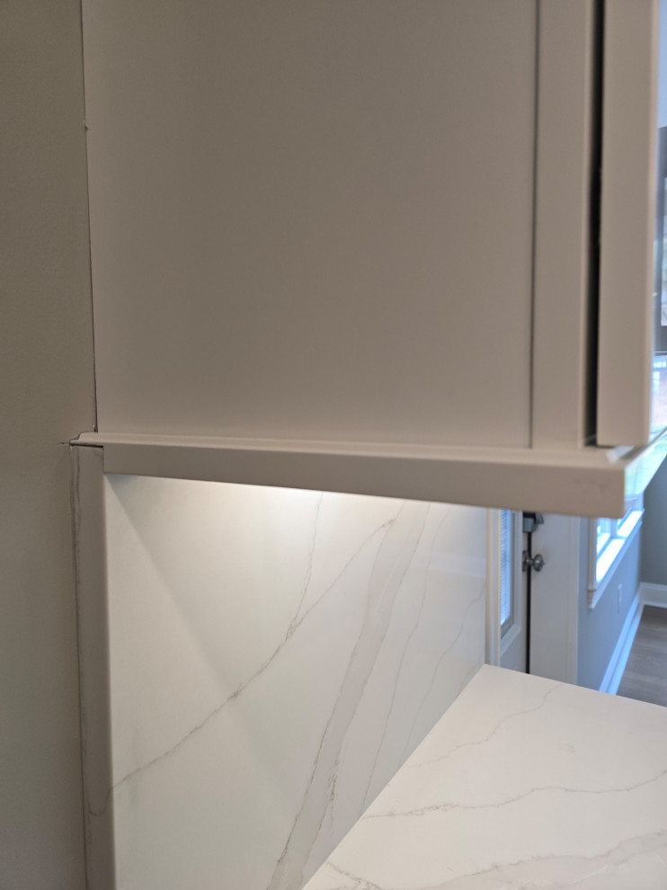 Large minimalist medium tone wood floor and brown floor kitchen photo with white cabinets, quartz countertops and white countertops