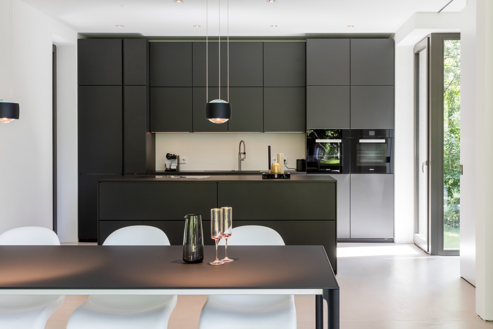 Design ideas for a mid-sized contemporary galley open plan kitchen in Hamburg with flat-panel cabinets, black cabinets, white splashback, with island, black appliances and white floor.
