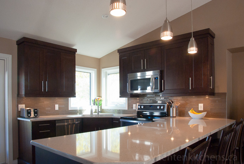 Open concept kitchen - mid-sized transitional u-shaped light wood floor open concept kitchen idea with an undermount sink, shaker cabinets, dark wood cabinets, quartz countertops, brown backsplash, glass tile backsplash, stainless steel appliances and a peninsula