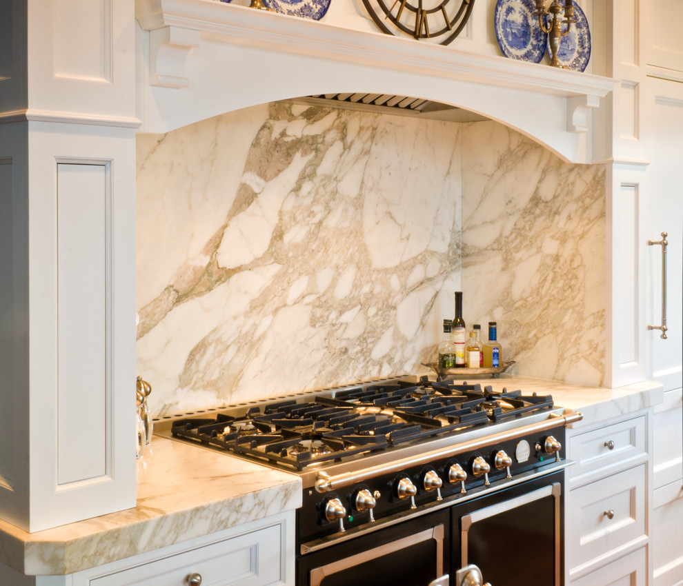 Photo of a mid-sized traditional u-shaped eat-in kitchen in Chicago with an undermount sink, beaded inset cabinets, white cabinets, marble benchtops, white splashback, stone slab splashback, black appliances, medium hardwood floors and with island.