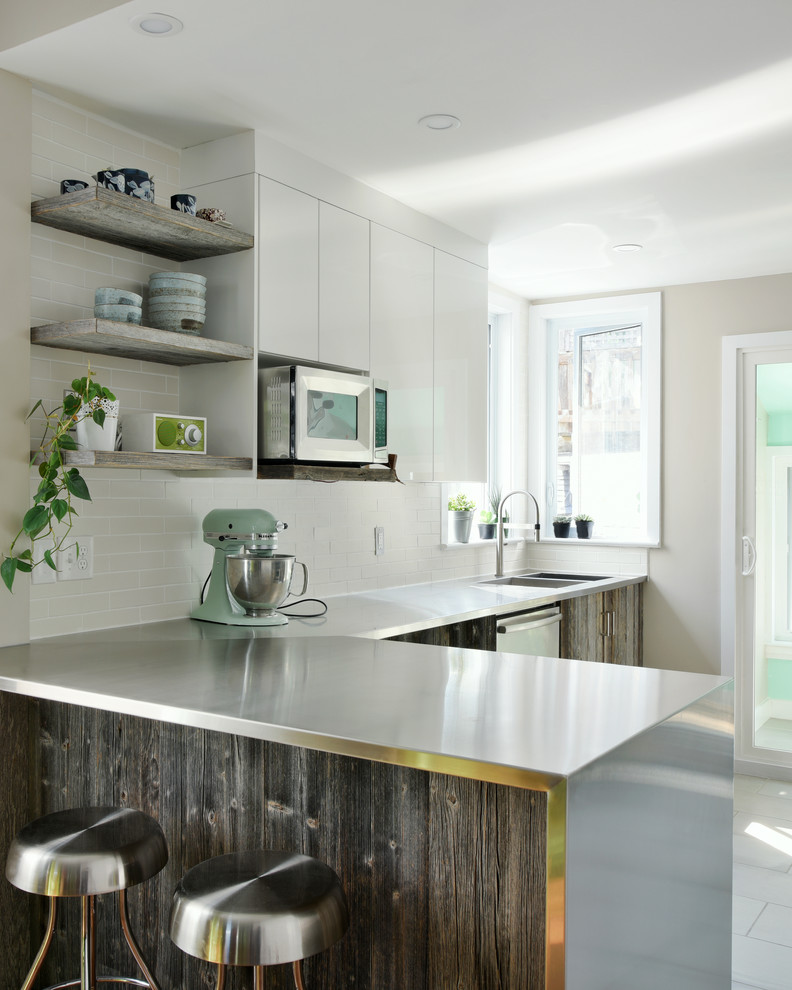 Design ideas for a mid-sized contemporary l-shaped kitchen in Ottawa with stainless steel benchtops, an integrated sink, flat-panel cabinets, distressed cabinets, white splashback, subway tile splashback, stainless steel appliances, porcelain floors and a peninsula.