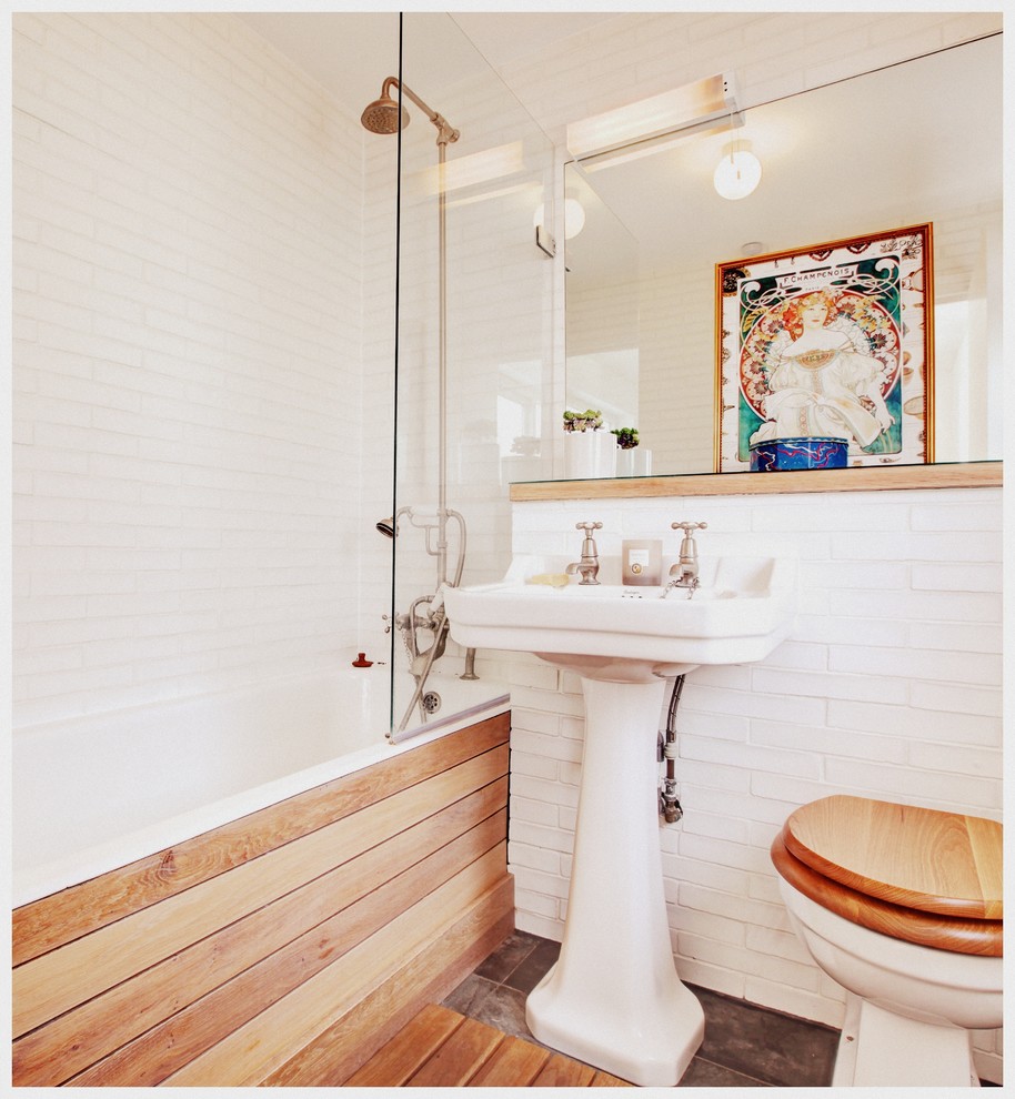Country bathroom in London with a pedestal sink, an alcove tub, a shower/bathtub combo, a two-piece toilet, white tile and white walls.
