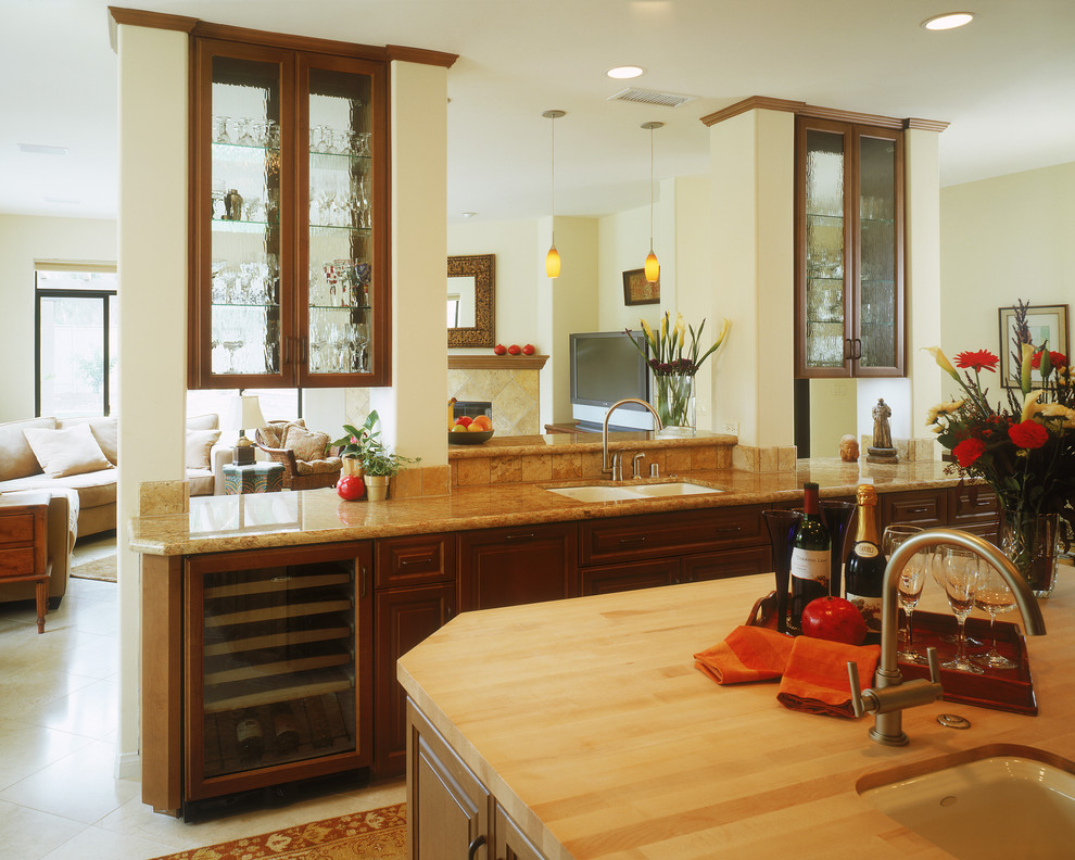 This is an example of a traditional open plan kitchen in San Diego with glass-front cabinets, wood benchtops, a double-bowl sink, dark wood cabinets, beige splashback, ceramic splashback, ceramic floors, with island and white floor.