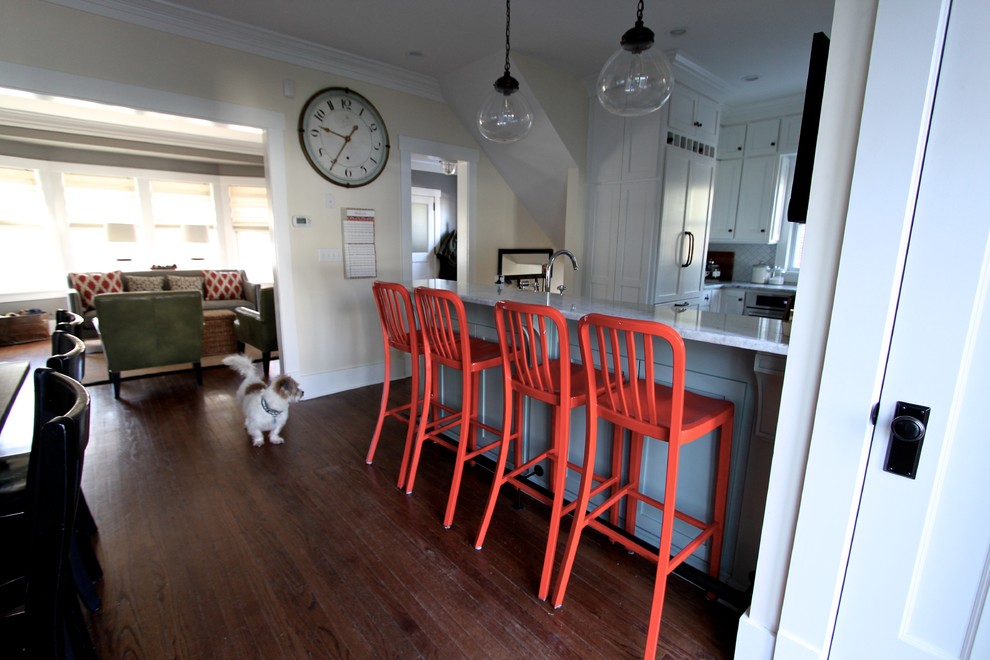 Example of a transitional medium tone wood floor kitchen design in Omaha with a farmhouse sink, shaker cabinets, white cabinets, quartzite countertops, white backsplash, ceramic backsplash, stainless steel appliances and a peninsula