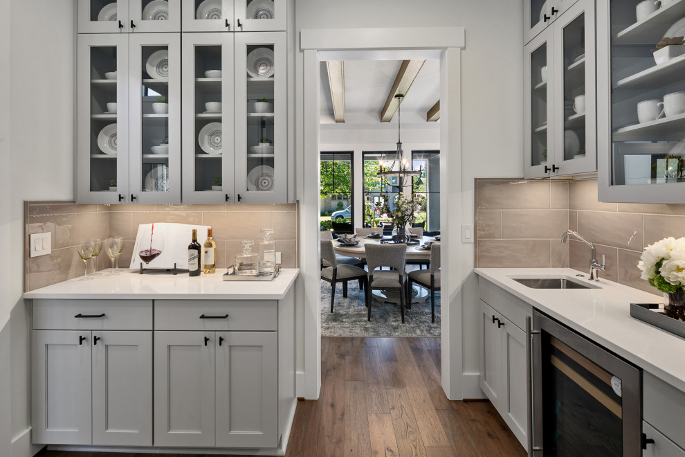 Inspiration for a mid-sized country l-shaped kitchen in Seattle with a drop-in sink, recessed-panel cabinets, grey cabinets, quartz benchtops, grey splashback, stainless steel appliances, medium hardwood floors, brown floor and white benchtop.