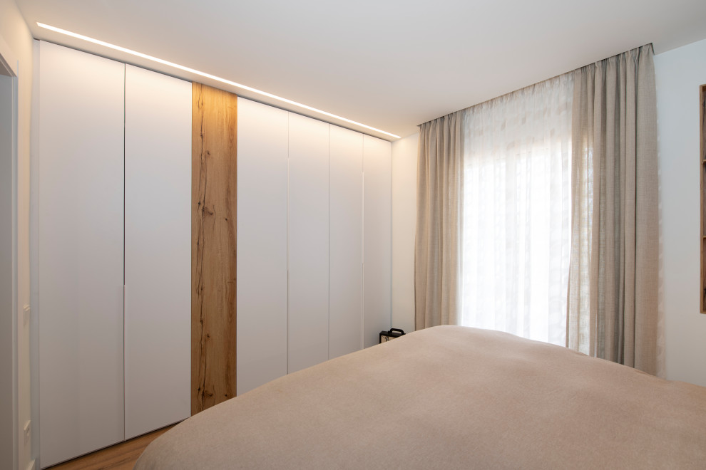 Idées déco pour une grande armoire encastrée scandinave neutre avec un placard à porte plane, des portes de placard blanches, sol en stratifié et un sol marron.