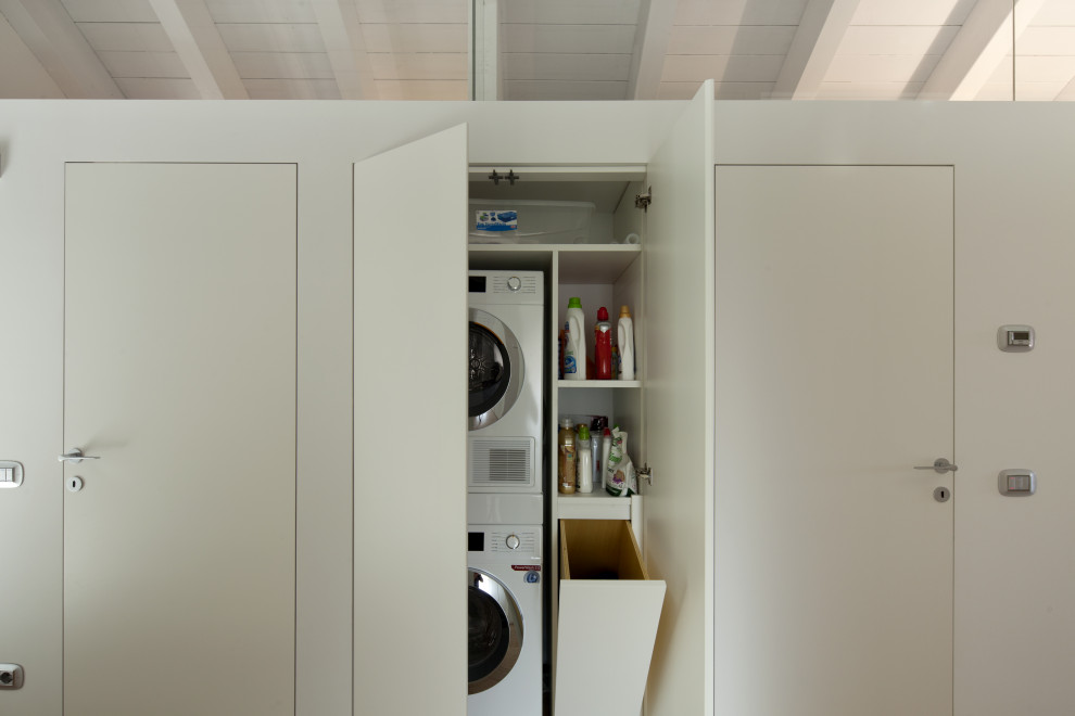 Design ideas for a small contemporary galley dedicated laundry room in Milan with flat-panel cabinets, white cabinets, laminate benchtops, white walls, light hardwood floors, a stacked washer and dryer, beige floor and white benchtop.