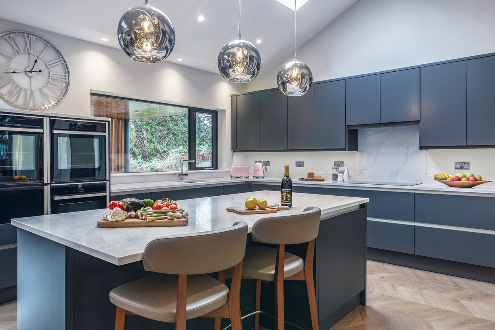 Photo of a contemporary l-shaped kitchen in Dublin with flat-panel cabinets, blue cabinets, black appliances, light hardwood floors, with island, beige floor and white benchtop.