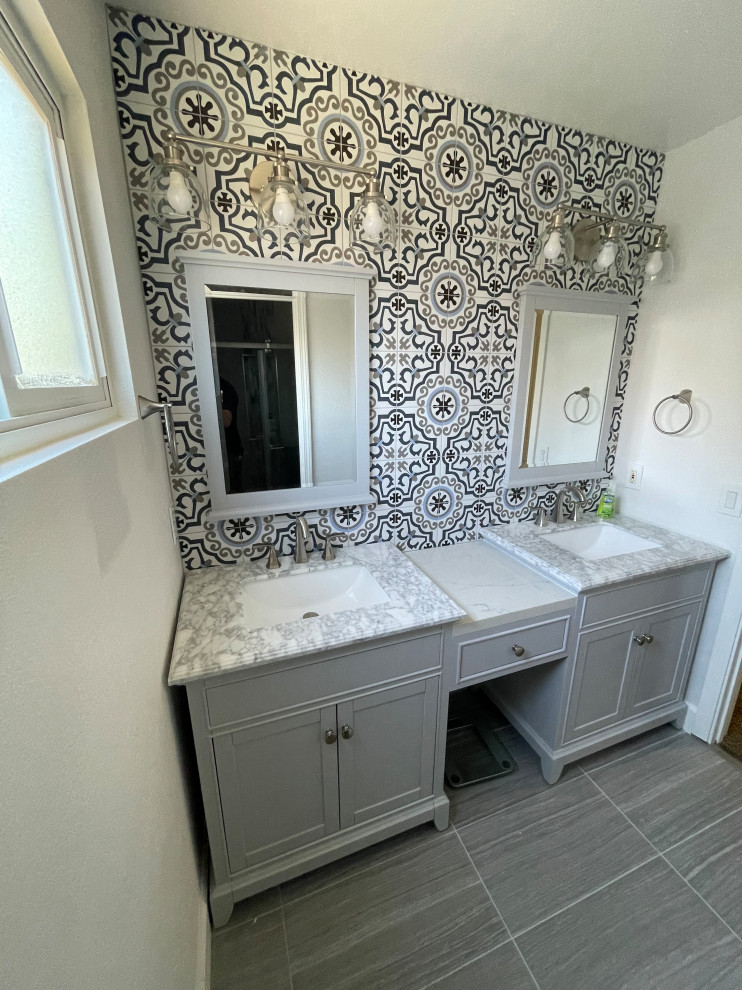 This is an example of a mid-sized transitional bathroom in San Francisco with furniture-like cabinets, grey cabinets, a drop-in tub, an alcove shower, a two-piece toilet, multi-coloured tile, porcelain tile, beige walls, porcelain floors, an undermount sink, engineered quartz benchtops, grey floor, a hinged shower door, multi-coloured benchtops, a niche, a double vanity and a freestanding vanity.