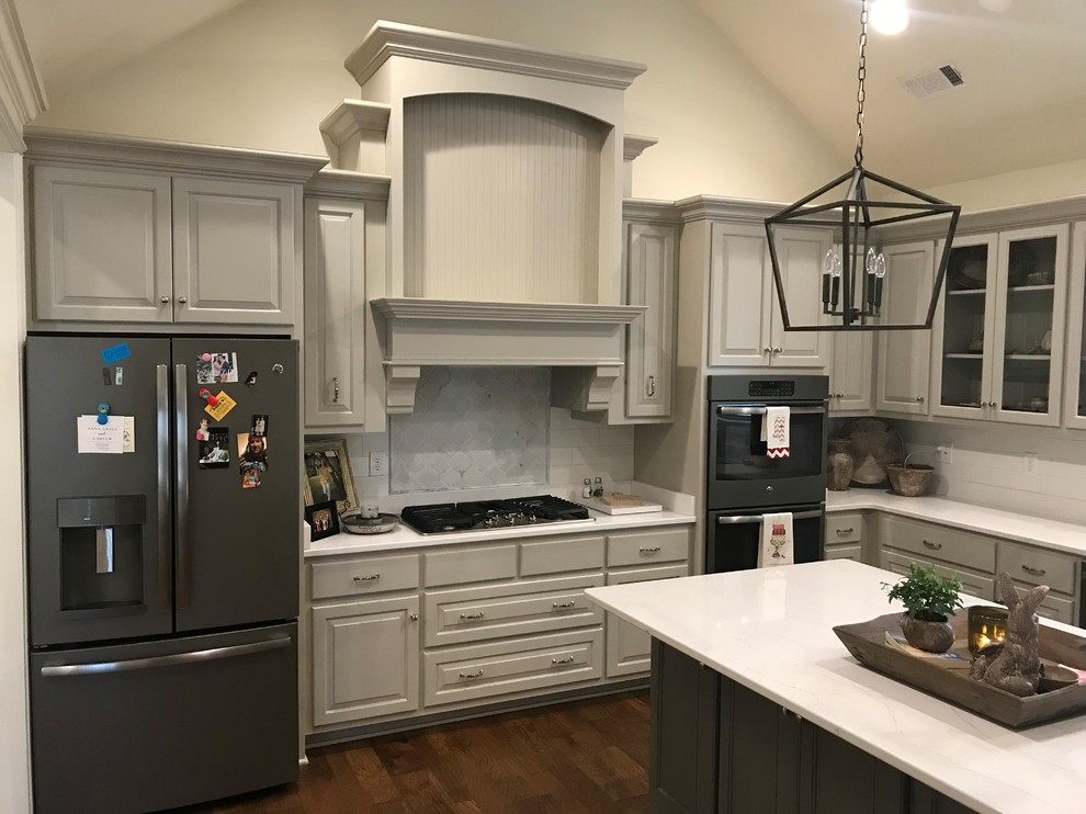 Large transitional l-shaped dark wood floor and brown floor open concept kitchen photo with a double-bowl sink, raised-panel cabinets, gray cabinets, white backsplash, subway tile backsplash, stainless steel appliances, an island and white countertops