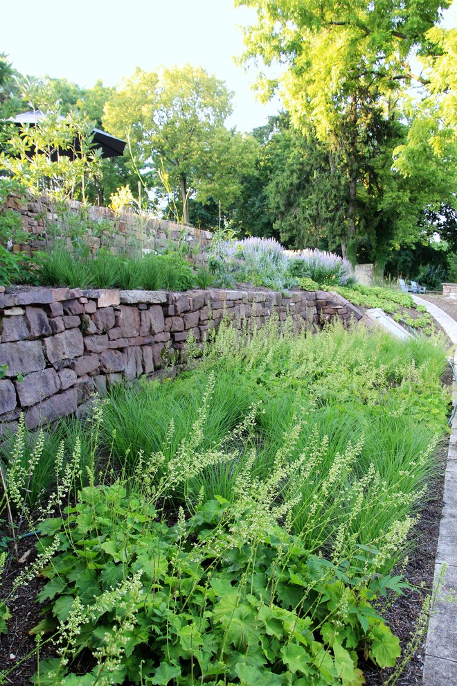 Photo of a mid-sized country sloped partial sun xeriscape in Philadelphia with a retaining wall and natural stone pavers.