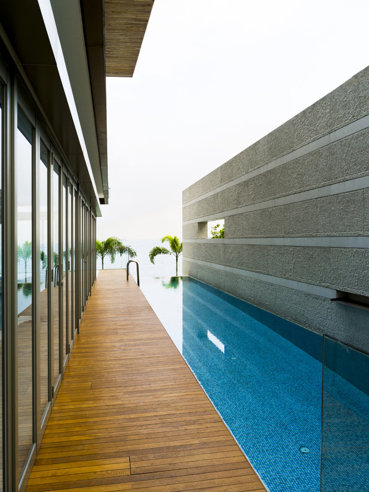 This is an example of a contemporary courtyard rectangular infinity pool in Singapore with a water feature and decking.