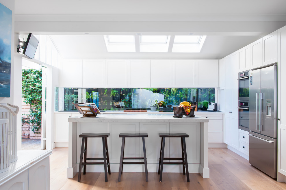 This is an example of a mid-sized transitional l-shaped kitchen in Sydney with white cabinets, with island, shaker cabinets, stainless steel appliances and medium hardwood floors.