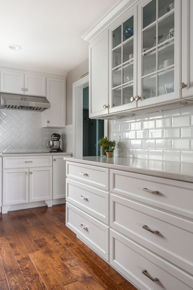 Inspiration for a large transitional l-shaped medium tone wood floor and brown floor eat-in kitchen remodel in Boston with an undermount sink, shaker cabinets, white cabinets, quartz countertops, white backsplash, subway tile backsplash, stainless steel appliances, an island and white countertops