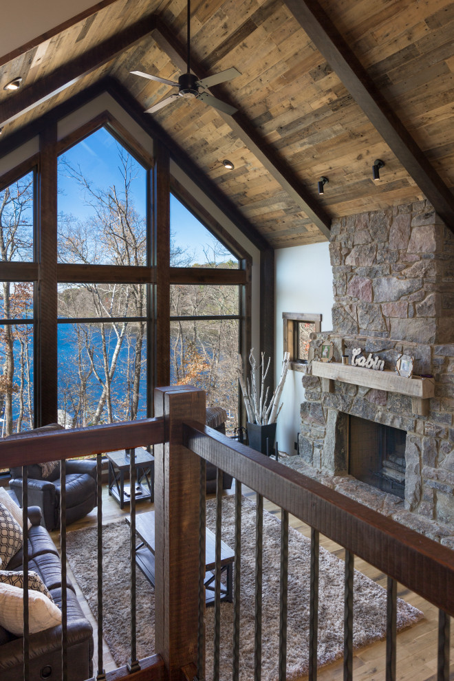 Cette photo montre un salon montagne avec un sol en bois brun, une cheminée standard, un manteau de cheminée en pierre et un plafond en bois.