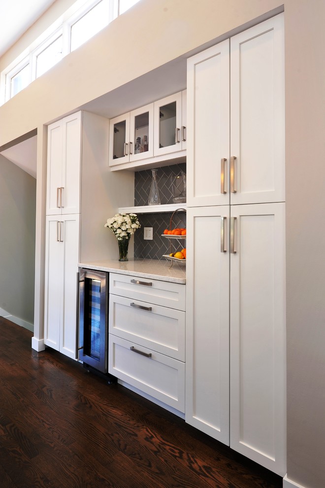 Design ideas for a mid-sized transitional single-wall wet bar in St Louis with an undermount sink, shaker cabinets, white cabinets, marble benchtops, grey splashback, subway tile splashback, dark hardwood floors, brown floor and grey benchtop.
