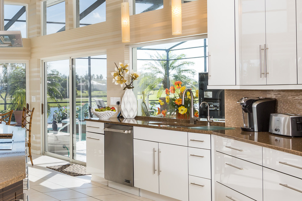 Photo of a large contemporary u-shaped eat-in kitchen in Miami with a drop-in sink, flat-panel cabinets, white cabinets, stainless steel appliances, ceramic floors, with island, quartz benchtops, brown splashback and matchstick tile splashback.