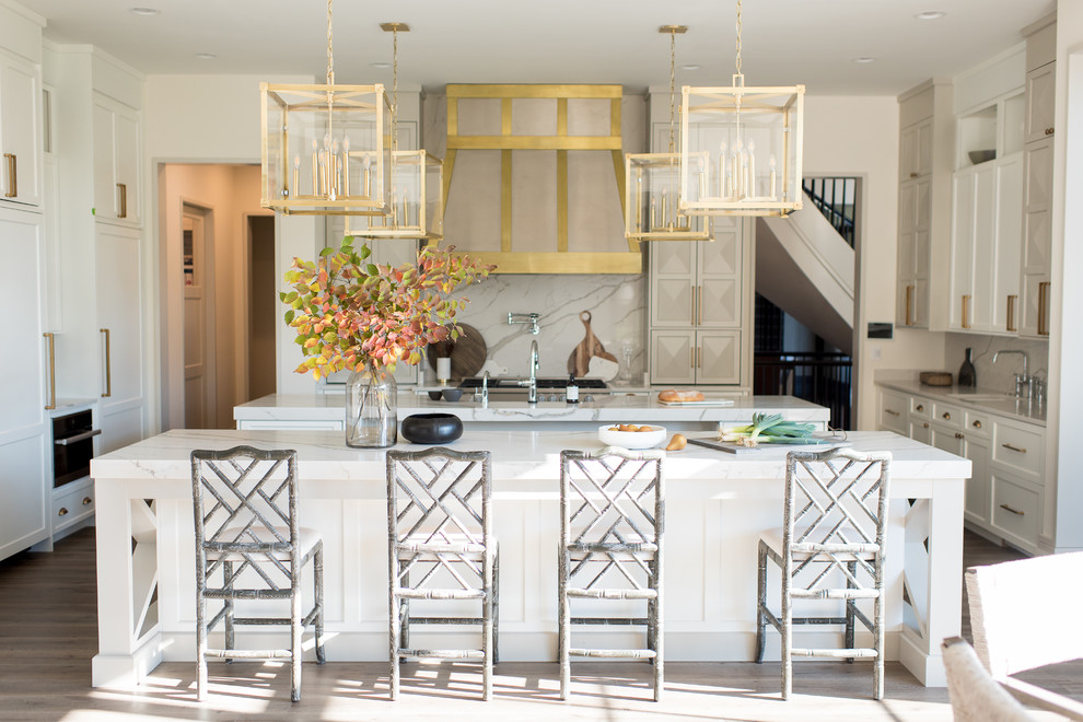Example of a huge transitional u-shaped medium tone wood floor and brown floor open concept kitchen design in Indianapolis with a farmhouse sink, shaker cabinets, white cabinets, quartzite countertops, white backsplash, stone slab backsplash, stainless steel appliances and two islands