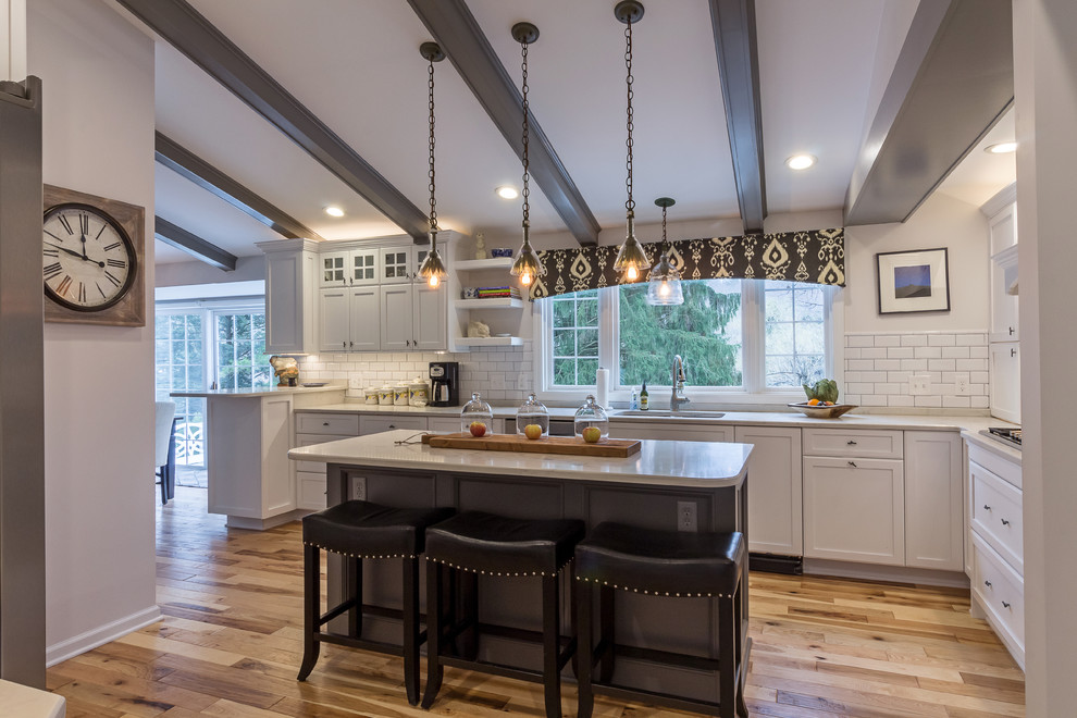 Inspiration for a large transitional u-shaped medium tone wood floor and brown floor enclosed kitchen remodel with an undermount sink, shaker cabinets, white cabinets, quartzite countertops, white backsplash, subway tile backsplash, stainless steel appliances and an island