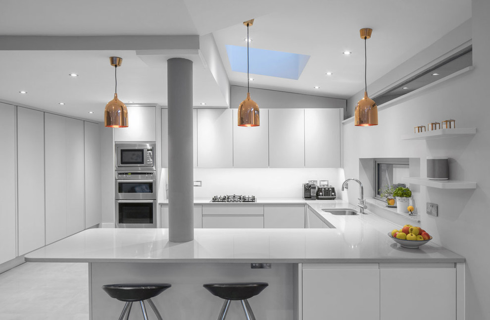 This is an example of a mid-sized contemporary u-shaped eat-in kitchen in Dublin with an integrated sink, shaker cabinets, white cabinets, solid surface benchtops, white splashback, panelled appliances, ceramic floors and a peninsula.