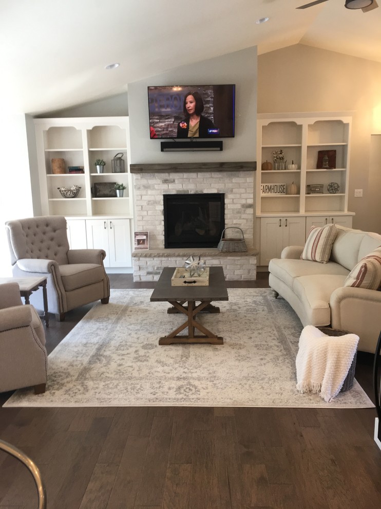This is an example of a large country open concept living room in Other with grey walls, medium hardwood floors, a standard fireplace, a brick fireplace surround, a wall-mounted tv and brown floor.