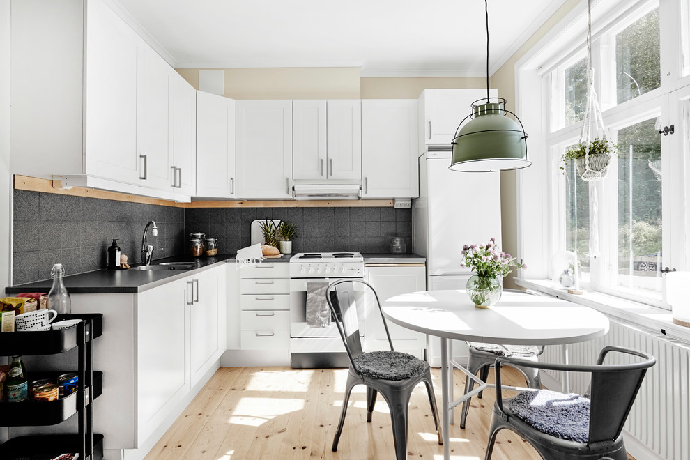Scandinavian l-shaped eat-in kitchen in Other with shaker cabinets, grey splashback, white appliances, light hardwood floors and beige floor.