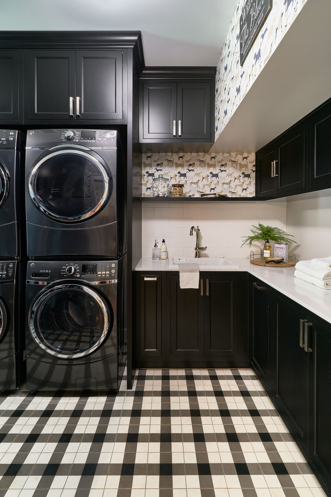 Design ideas for a traditional l-shaped dedicated laundry room in Austin with a drop-in sink, black cabinets, a stacked washer and dryer, white benchtop and recessed-panel cabinets.