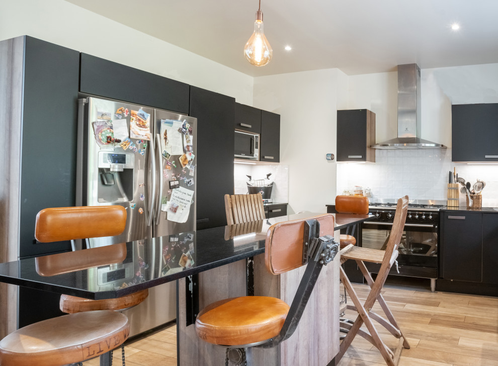 This is an example of a large urban u-shaped kitchen with a built-in sink, beaded cabinets, black cabinets, marble worktops, white splashback, terracotta splashback, black appliances, medium hardwood flooring, an island, brown floors and black worktops.