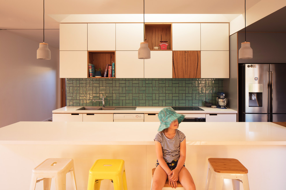 Photo of a mid-sized contemporary galley eat-in kitchen in Melbourne with a double-bowl sink, white cabinets, quartz benchtops, green splashback, ceramic splashback, stainless steel appliances, light hardwood floors, with island and white benchtop.