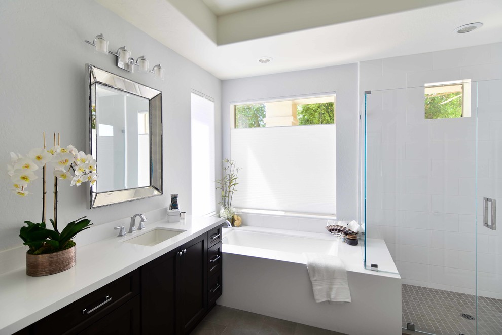This is an example of a mid-sized transitional master bathroom in Phoenix with recessed-panel cabinets, black cabinets, an undermount tub, a corner shower, white tile, ceramic tile, grey walls, ceramic floors, an undermount sink, engineered quartz benchtops, grey floor, a hinged shower door and white benchtops.
