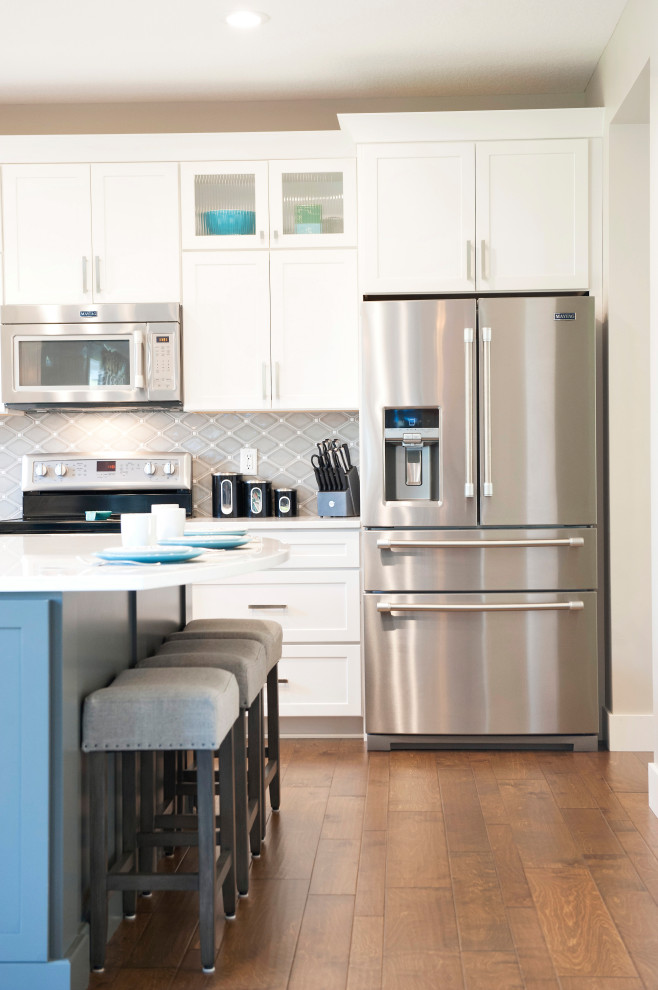 Eat-in kitchen - mid-sized transitional l-shaped medium tone wood floor and brown floor eat-in kitchen idea with an undermount sink, shaker cabinets, white cabinets, quartz countertops, gray backsplash, mosaic tile backsplash, stainless steel appliances, an island and white countertops